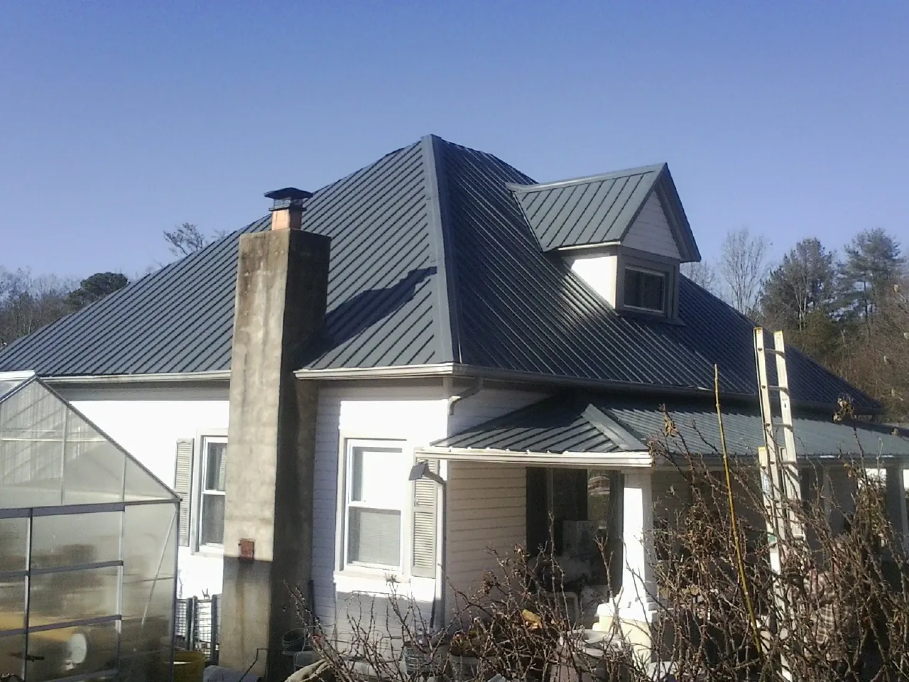 Dark blue standing seam metal roof on a white farmhouse with dormer — Slate & Tile Roof Repair by Roofing Brothers in Malvern