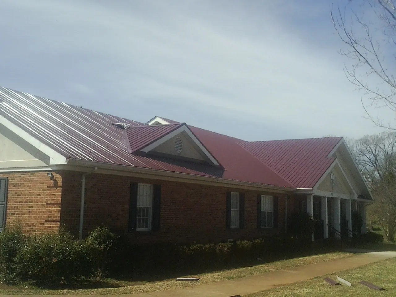 Red metal roof with gabled entries on a long brick building, from a Hail Damage Roof Repair job in Malvern
